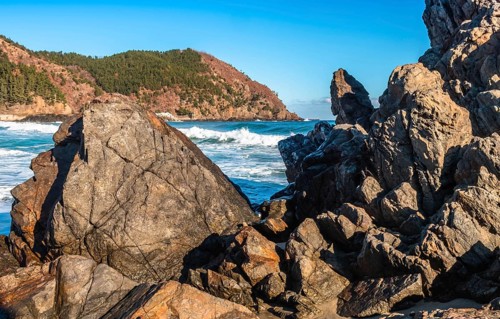 Foamy waves hitting the rocky shores of a vibrant blue sea on a sunny day with a clear sky, in