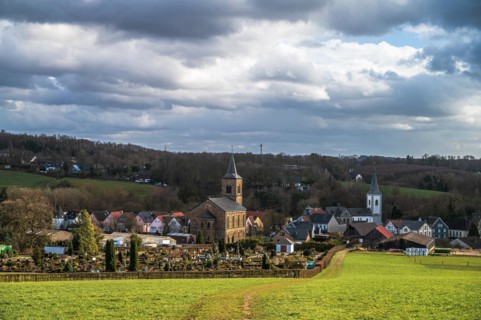 Picturesque view of a quiet village embedded in the green, rural landscape under a cloudy sky,