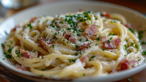 A close-up of fettuccine pasta garnished with Parmesan cheese, bacon bits and parsley on a white