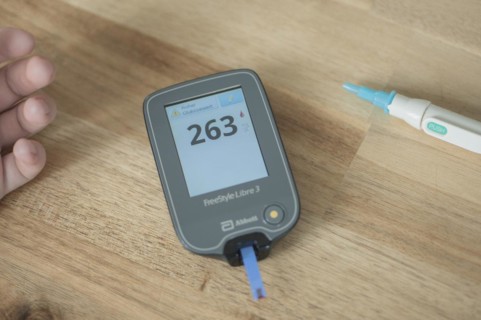 Blood glucose meter with test strips and a drop of blood lies in the centre of a wooden table, high