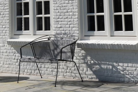 A black metal bench in front of a white wall casts a shadow in the sunlight
