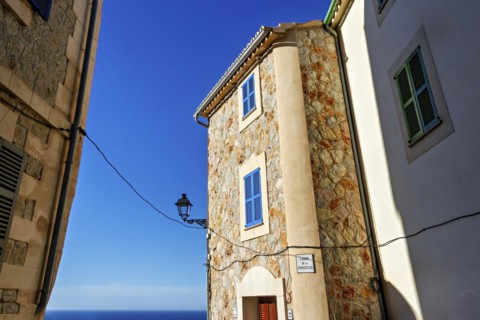 A picturesque stone building with blue shutters beside a cobblestone street under a blue sky,