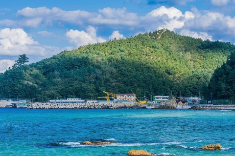Scenic view of a coastal village by the sea with mountains and blue sky, in South Korea
