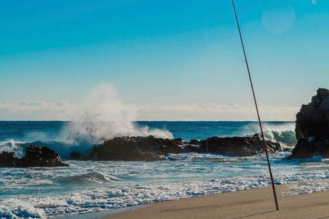A dramatic maritime scene with a fishing rod overlooking waves crashing onto rocky shores, in South