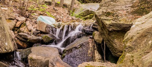 White plastic bag full of trash in stream of water cascading over large rocks and boulders in South