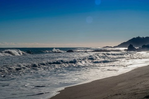 Rugged seascape with waves under bright morning sun crash onto beach and rocks under a beautiful