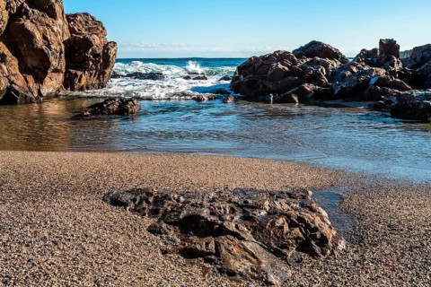 A serene beach scene with waves crashing against large rocks under a clear blue sky, in South Korea