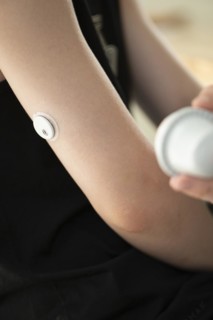 Child holding a setting aid for a glucose sensor, the sensor has been attached to the child's arm,