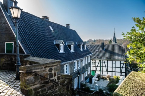 View of an alley with historic half-timbered houses and a church spire in the background,