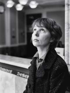 Black and white image of a contemplative woman gazing upwards, standing by a marble counter
