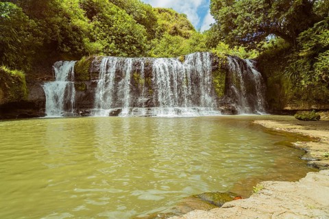 Landscape of a waterfall with trees and blue sky in the background and water basin in the