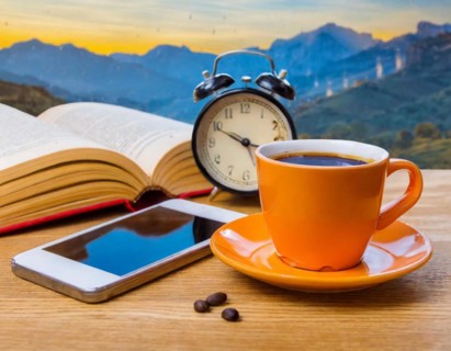 A coffee cup, an alarm clock and a smartphone lie on a table with a mountain view, AI generated, AI