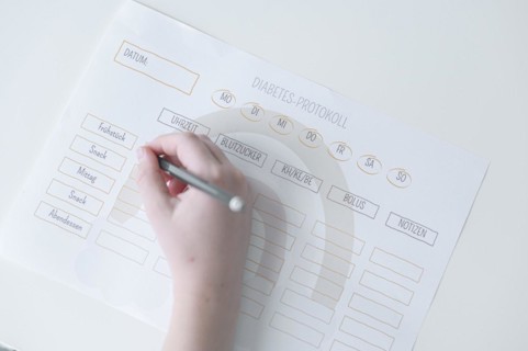 Diabetes log, daily log of food and insulin administration, food log, hand of a child holding a pen