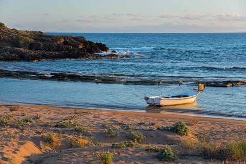 Tranquil scene of a single boat on the coastline with rocks in the soft evening light, Finikounda,