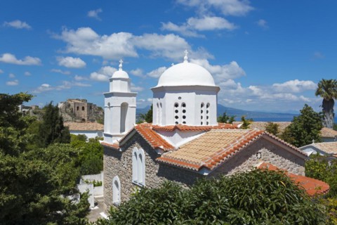 Bright church with white domes, surrounded by green trees and red roofs, viewpoint on the left,