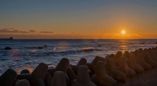 Tranquil sunset with orange sky over sea and tetrapods lined up on the coast, in South Korea