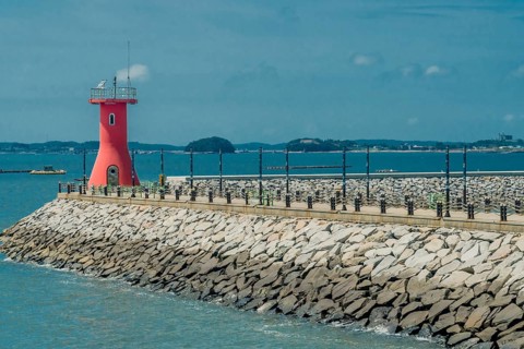 Red lighthouse on end of concrete pier in seaside fishing port in South Korea