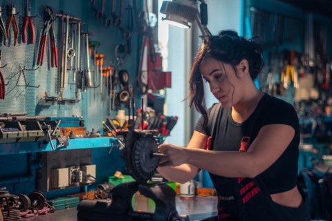 Serious young mechanic concentrating on repairing a scooter engine part in a vise in a well-lit