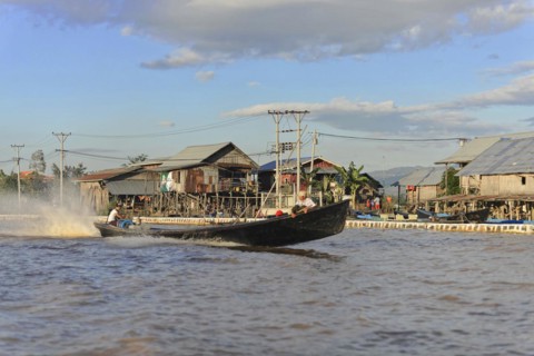 Fishing boat passes stilt houses of a waterfront village, Pindaya, Inle Lake, Myanmar, Asia