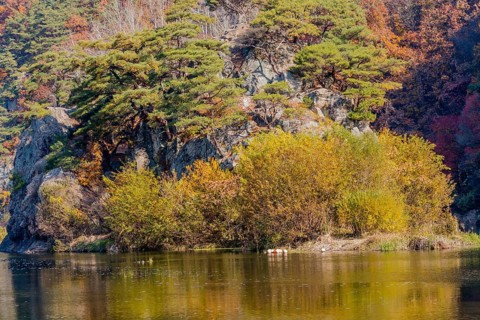 Autumnal trees by the water with cliffs in the background, reflecting on the surface, in South