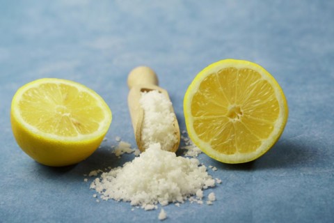 Lemon cut in half with salt on a wooden spoon on a blue background and copy space