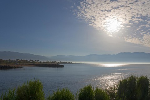 A peaceful sunrise over a coastal landscape with clouds in the sky and calm sea, mouth of the river