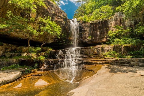 A tall waterfall plummets down a rocky cliff surrounded by vibrant green foliage, in South Korea
