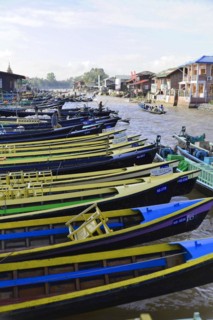 Row of colourful boats on a river bank with houses in the background, Pindaya, Inle Lake, Myanmar,