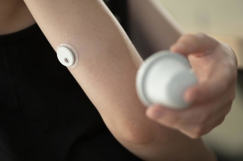 Child holding a setting aid for a glucose sensor, the sensor has been attached to the child's arm,