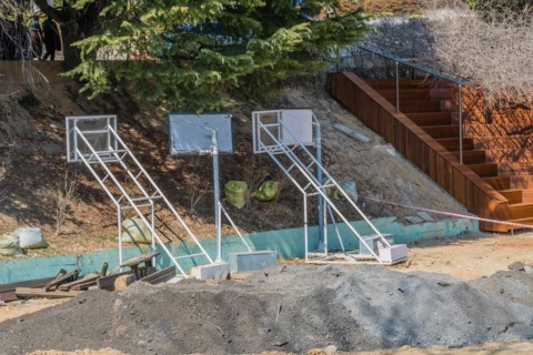 Construction equipment and a pile of earth sit near wooden stairs under a bright sun, in South
