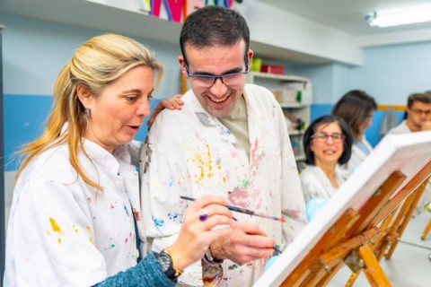 Instructor helping a disabled man during painting class in a center for people with special needs