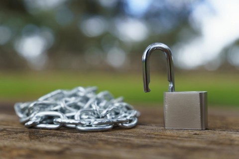 Close-up of an open padlock next to a chain strung on a wooden table in a field with an