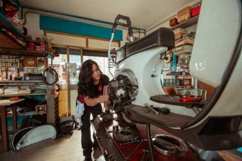 Determined woman mechanic inspecting the front of a white old scooter during an engine check,