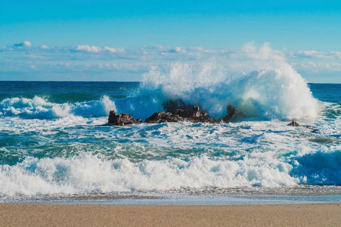 Dynamic white waves collide with coastal rocks on a sunny day with a vibrant blue ocean, in South