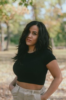 Cheerful hispanic young sensual Woman in a black shirt and beige pants outdoors with hands on hips