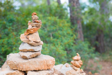 Carefully stacked, slightly red stones form a stone figure, cairn, waymark, marker in the forest,