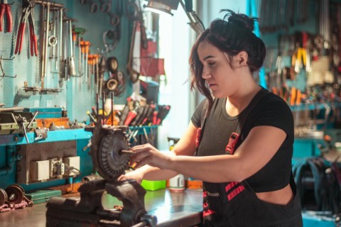 A woman is attentively working on a mechanical piece at a tidy workshop bench, a complete tool
