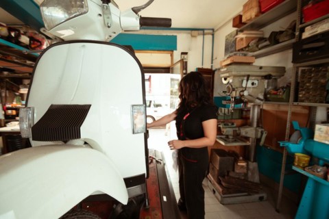 Side view of a mechanic doing precision work on a vintage scooter, latino female in traditional