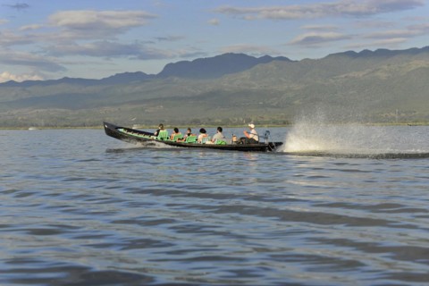 Motorboat with passengers racing on a calm river with mountain backdrop, Inle Lake, Myanmar, Asia