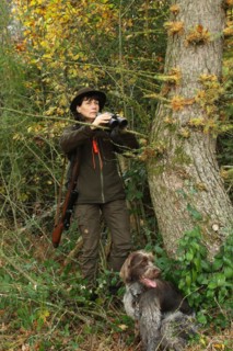 Huntress with hunting dog Griffon, binoculars and rifle at the edge of the forest, Allgaeu,