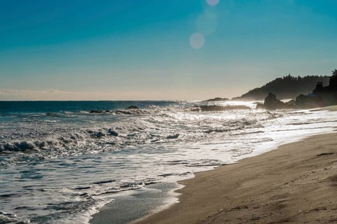 Rugged seascape with waves under bright morning sun crash onto beach and rocks under a beautiful
