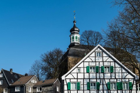 A medieval church behind a classic half-timbered house with a slate-covered roof, Graefrath,