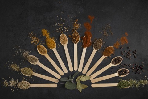 Colourful spices arranged in fan-shaped spoons on a dark background