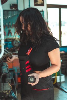 Young confident skilled hispanic long haired brunette woman in a mechanic's apron is examining a