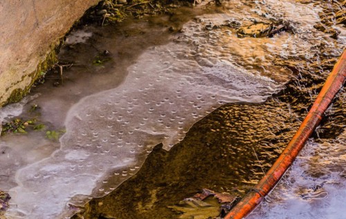 Frozen water with air bubbles trapped under the surface near a rusty pipe, in South Korea