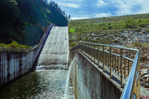 Dam with a sheet of water flowing over its edge, surrounded by mountains, in South Korea