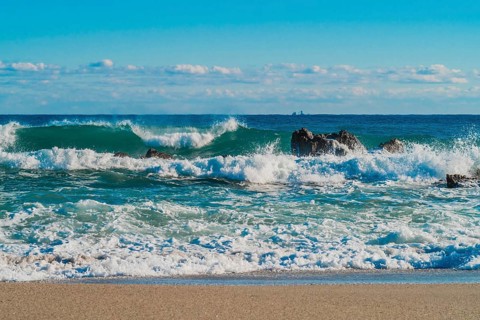 Foamy waves break on rocks with a clear horizon beyond under a deep blue sea, in South Korea