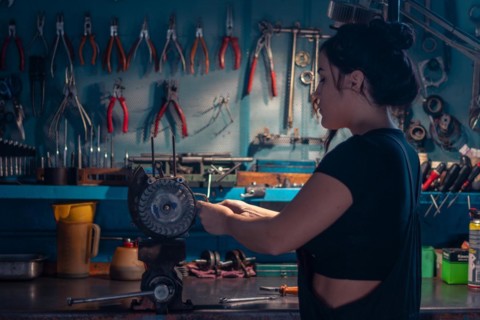 Mixed-race hispanic young Female mechanic, wear black overall, focused on an motorcycle part in a