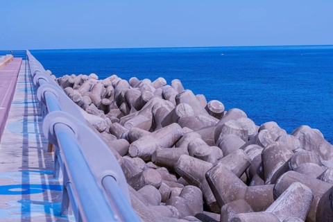Concrete tetrapods line a coastal walkway under clear skies, with a vivid blue ocean in the
