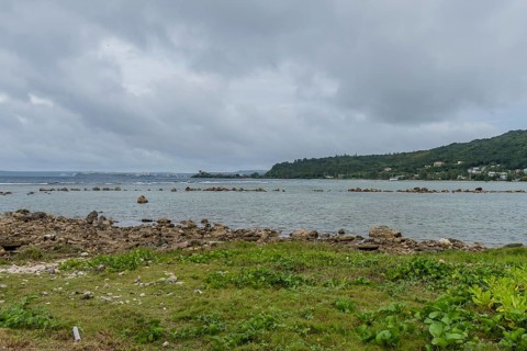 Seascape of rocky shoreline on a cloudy day with buildings on tree lined shore in the distance in